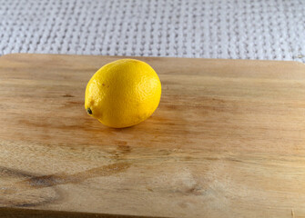 A single yellow lemon rests on a smooth, light-colored wooden surface. The vibrant fruit appears fresh and perfect for adding flavor to meals or drinks