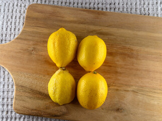 Fresh, vibrant yellow lemons sit atop a light wooden cutting board. The scene is well lit, highlighting their shiny skin and natural color, perfect for cooking or garnishing