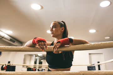 Focused female boxer resting on ring during training session in a gym setting
