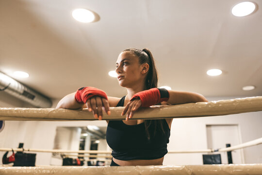 Focused female boxer resting on ring during training session in a gym setting