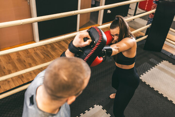 Female boxer practices punches while training with a coach in a gym setting during the day