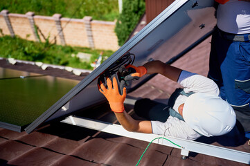 Worker building solar panel system on metal rooftop of house. Man technician preparing to install photovoltaic solar module outdoors. Alternative, green and renewable energy generation concept.