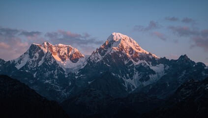 Snow-capped mountain peaks illuminated by the warm glow of sunrise against a clear blue sky, showcasing a stunning display of natural beauty, creating a tranquil and breathtaking landscape scene.