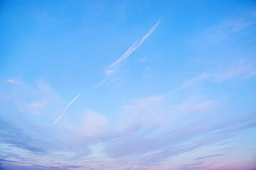 Clear blue sky with soft clouds and airplane contrails at sunset