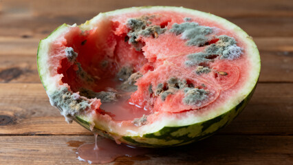 Half of a rotten watermelon with mold growth on the flesh, placed on a wooden surface