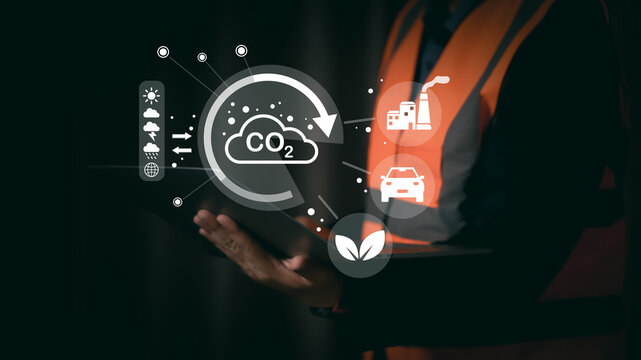 Engineer in safety vest using tablet with CO2 emission and sustainability icons, representing carbon footprint, environmental impact, green industry, renewable energy, and eco-friendly technology.