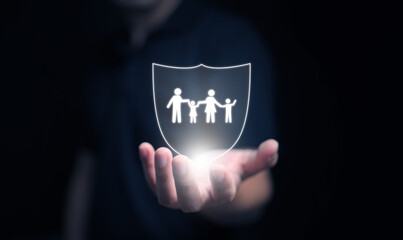Hand holding glowing shield with family icon inside, representing insurance, safety, financial protection, security, healthcare, and strong family support concept.