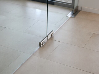 glass door with a metal hinge or clamp mechanism attached to a tiled floor, featuring smooth,...