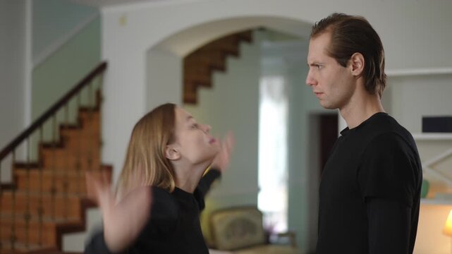 Man and woman standing close and arguing emotionally in a home interior. The woman gestures expressively while the man looks serious, showing tension and unresolved conflict in their relationship