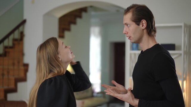 Man and woman stand face to face in heated argument, gesturing and showing tension. Their serious expressions reveal emotional distance and inability to listen during conflict in relationship