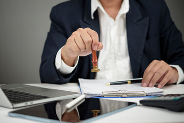 Manager hand holding a stamp for final approval business document. Concept of deal confirmation, project authorization, corporate governance, and certified paperwork with laptop and tablet on desk.