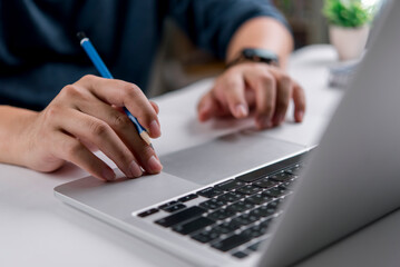 Designer or student hand holding pencil working on laptop at desk. Concept for creative process, project planning, online learning, e-learning, brainstorming ideas, or working from home office.
