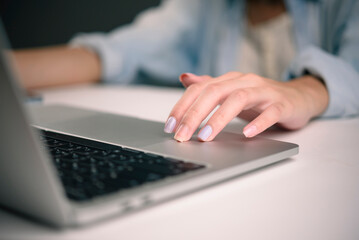Close up female hand using laptop touchpad for online shopping or browsing website. Woman with nail art clicking and navigating e-commerce store. Digital lifestyle and online purchasing concept.