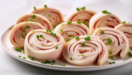 close up of multiple delicate creamy chicken and ham rolls on a white plate with some chives sprinkled over them