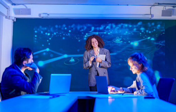 Mid adult businesswoman doing AI presentation to team in the modern office