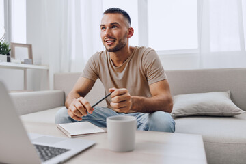 A thoughtful man sits in a bright, modern living room, contemplating ideas while holding a pencil. He showcases a relaxed yet focused expression, embodying creativity.