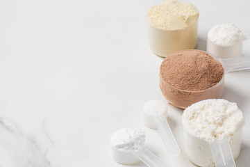 Assorted protein powder and supplement scoops on white marble background for nutrition and fitness