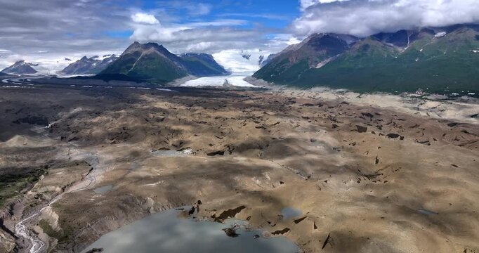 Vegetation less rocky landscape with some water from melting ice. Striking rocks coated with clouds at backdrop. Alaska, USA. Aerial view.