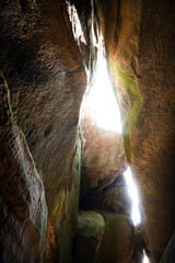Bright sunlight shines through narrow rock formations in a scenic cave