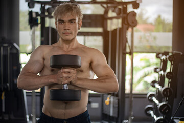 Athletic shirtless handsome young man, muscular young men are exercising with weights in a gym.
