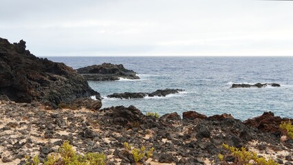 Volcanic coastline featuring natural seawater pools with access structures, providing a popular destination for naturists and tourists seeking open-air living experiences