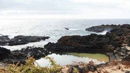 Natural pool of Charco del Palo, offering a serene swimming experience, nestled within a nudist village on a rugged volcanic coastline, embodying freedom and relaxation for naturism tourism