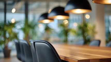 A spacious modern workspace features a long wooden table surrounded by sleek black chairs. Stylish pendant lights hang above, illuminating the area while plants add a touch of nature
