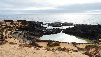 Rocky coastline with a tranquil natural pool reflecting the sky, clear tide pool waters and secluded shore ideal for naturism, relaxation and summer ocean recreation