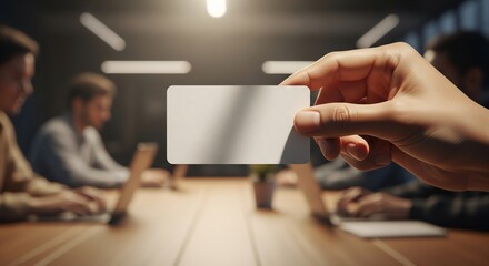 Hand holds blank card over conference table during business meeting in modern office, emphasizing potential for connection and opportunity.