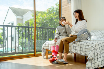 Asian mother sit on bed next to her daughter and give a glass of mild to her child during practice fencing sport in bedroom with soft morning light and happiness.