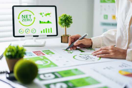 Business professional analyzes net zero ESG sustainability report environmental data charts for corporate responsibility modern office desk