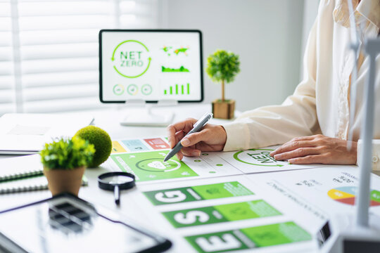 Business professional analyzing ESG net zero corporate sustainability strategy environmental data planning at office desk - Powered by Adobe
