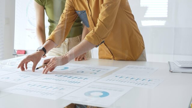 Business professionals analyzing financial reports, pointing at charts during collaborative meeting, discussing data with focused professional demeanor - Powered by Adobe