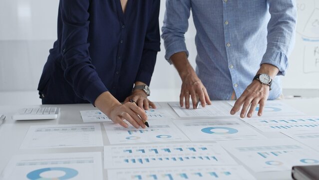 Professional team reviewing financial documents, pointing at charts on desk, collaborating to analyze data and strategize business growth. Business people concept