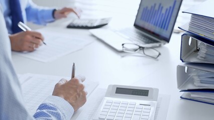 Auditors collaborating in modern office, analyzing financial documents and using calculator with a...