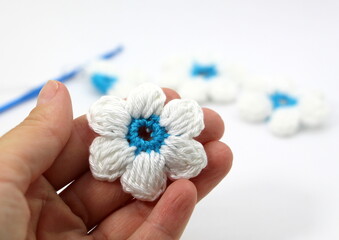 A flower with six white petals and a blue center crocheted on a white background.
