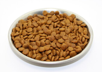 Dry balanced food for cats or dogs in a metal bowl on a white background.