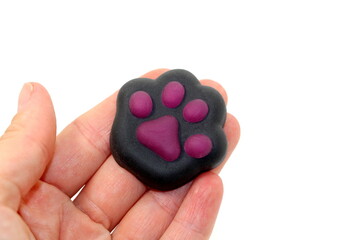 A trendy anti-stress toy, a black cat paw with purple pads, lying in a hand on a white background.