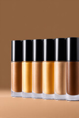 Row of liquid foundation bottles with makeup concealer for variety of skin tones. Cosmetic product for beauty and diversity against brown background for flawless face