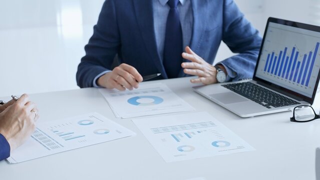 Businesspeople colleagues are reviewing financial data, analyzing charts and graphs, pointing at laptop screen during corporate meeting. Business people and finance concept