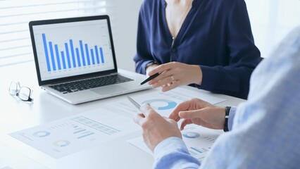 Businessman and business woman reviewing financial documents, collaborating over laptop screen, analyzing market charts for strategic corporate planning. Businesspeople and finance concept