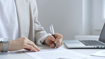 Businesswoman signing a contract at office desk, surrounded by a laptop and documents, exemplifies focus and commitment. Business people