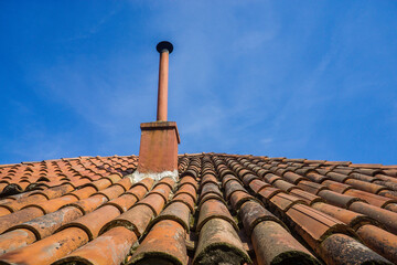 Close up of red clay tile roof and chimney against clear blue sky.