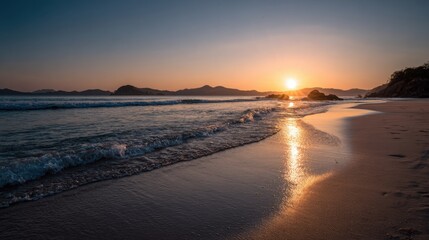 Golden sunlight touches the sandy shore as waves gently lap at the beach. Distant mountains create a peaceful backdrop during the tranquil evening hours.