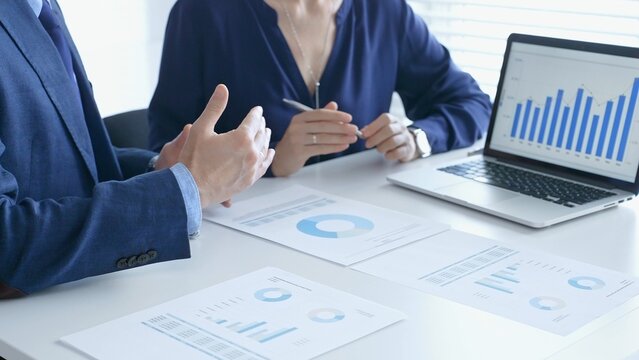 Businessman and business woman reviewing financial documents, collaborating over laptop screen, analyzing market charts for strategic corporate planning. Businesspeople and finance concept