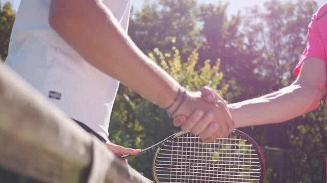 Two athletes shake hands over a tennis net on a sunny day, symbolizing sportsmanship and camaraderie on a lush outdoor court, highlighting competition and mutual respect, captured in a close-up.