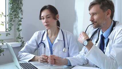 Two doctors are studying medical charts on a laptop, discussing patient data in a hospital or clinical setting. Medicine and healthcare concept.
