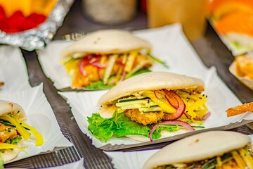 Delicious Asian-style bao buns filled with crispy chicken, fresh vegetables, and vibrant sauces, beautifully arranged on a textured surface for an appetizing culinary presentation