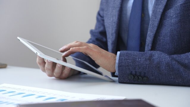 Businessman is using a digital tablet to analyze financial data, working with modern technology in the office for strategic corporate decision making and workflow optimization. Business people concept - Powered by Adobe