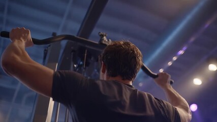 Man in a gym using a cable machine, pulling a wide bar with both hands during a lat pulldown/back workout.